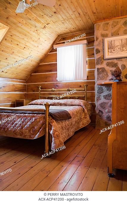 Antique brass bed and dresser in an upstairs bedroom in a 1978 reproduction of an old Canadiana cottage style log and fieldstone residential home, Quebec