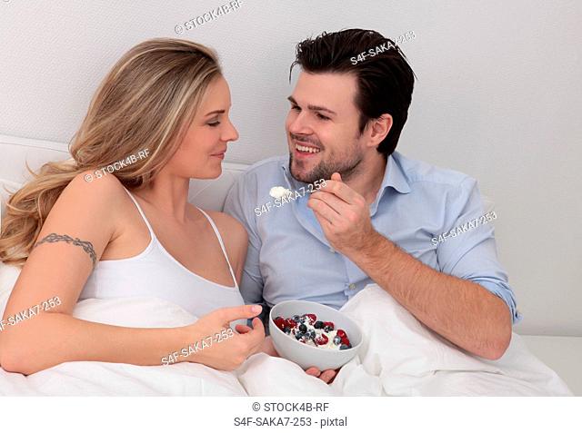 Couple eating berries from bowl in bed