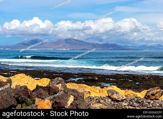 Panoramic view at the coastline of Corralejo on canary island Fuerteventura, Spain with lava rocks and rough sea with waves and canary island Lanzarote in the...