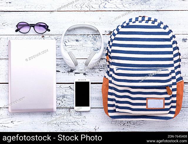 Necessary summer objects for vacation are represented on wooden background. Digital devices like laptop, smart phone and earphones are for communication with...