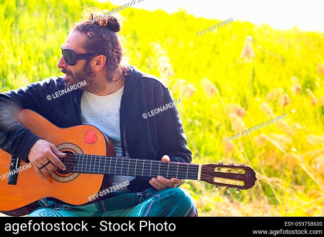 Hippy man with beard and glasses playing guitar outdoors on the grass. High quality photo
