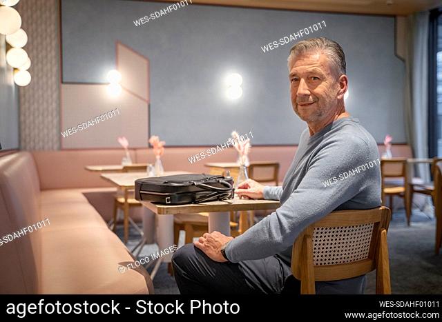 Smiling businessman with briefcase sitting at modern cafe