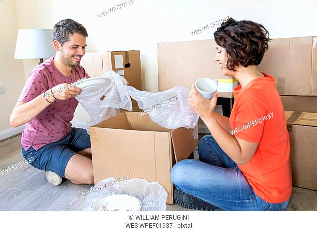 Happy couple moving into new home unpacking cardboard box