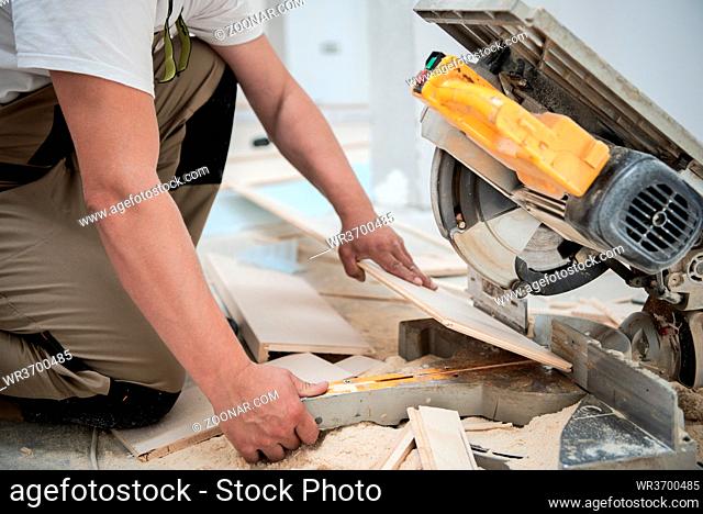 professional worker cutting plank with electrical circular saw during installation a new laminated wooden floor in a unfinished apartment