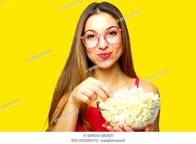 Girl with positive emotion holding pop corn and watching comedy movie isolated on yellow background studio portrait