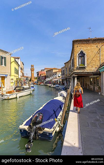 Young woman at a canal, houses and boats at the canal Rio del Vetrai, bell tower St. Stefano, Murano, Venice, Veneto, Italy, Europe