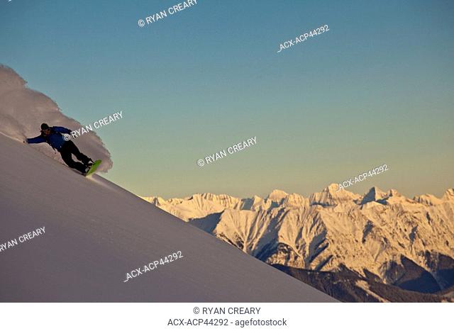 A snowboarder slashes a turn in the alpenglow, Kicking Horse Backcountry, Golden, Britsh Columbia, Canada