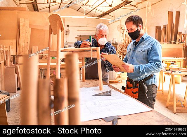 Zwei Handwerker mit Mundschutz wegen Covid-19 als Möbeltischler bei der Arbeit