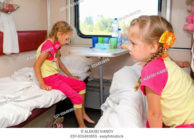 Two girls sisters on the train on the lower ground in the second-class compartment wagon