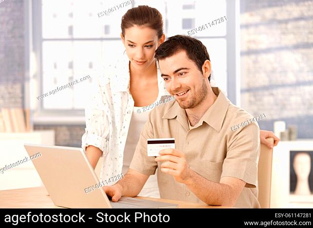 Happy couple using laptop, shopping online at home, using credit card