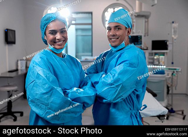 Smiling diverse male female surgeons with face masks and protective clothing in operating theatre