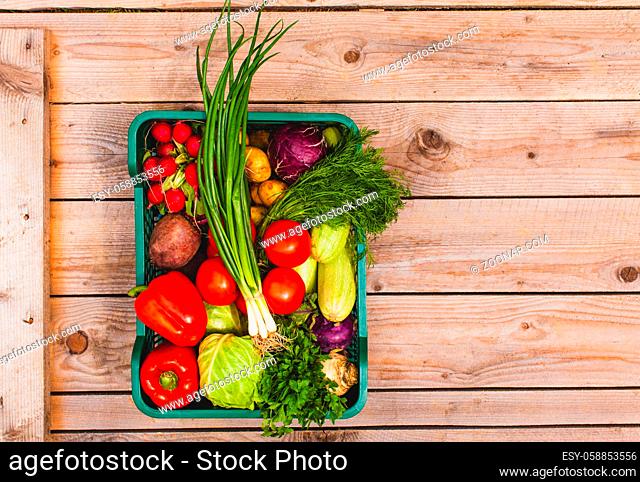 Top view of fresh vegetables in a box on the wooden board with copyspace on the right side