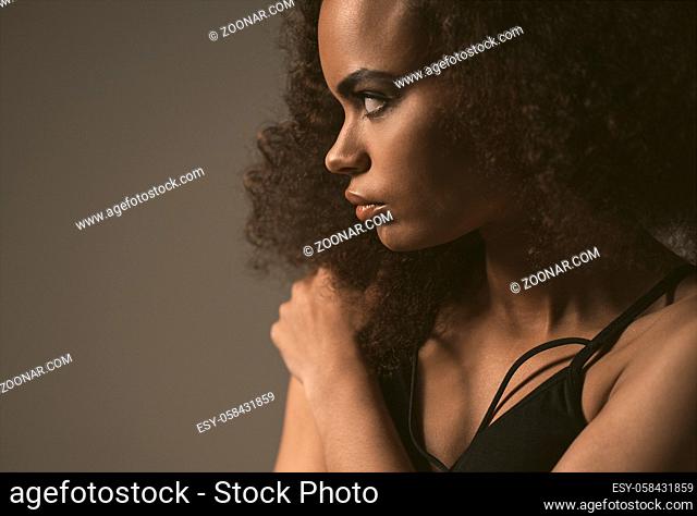 Tender African American girl standing in black top isolated on grey background. Human emotions, facial expression concept