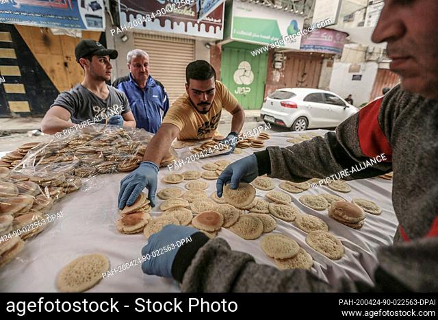 24 April 2020, Palestinian Territories, Gaza: Palestinians vendors prepare traditional Ramadan pancakes known as 'Qatayef' in a local market as Muslims shop for...