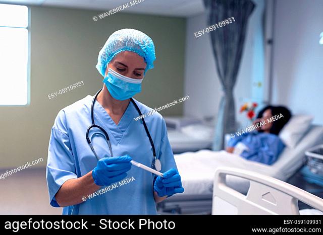 Caucasian female doctor in hospital wearing face mask and surgical gloves holding swab test