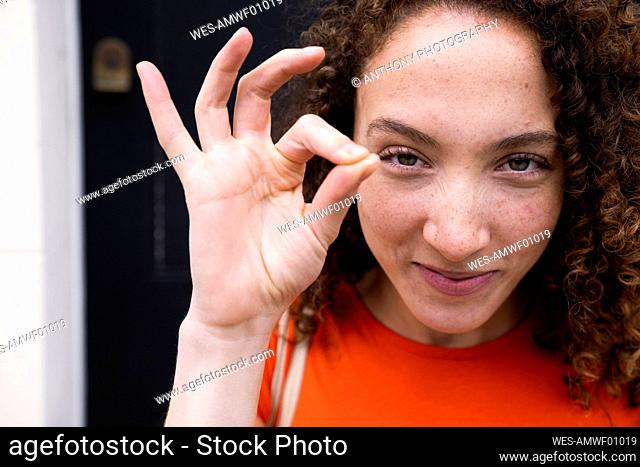 Smiling woman showing OK sign gesture in front of door
