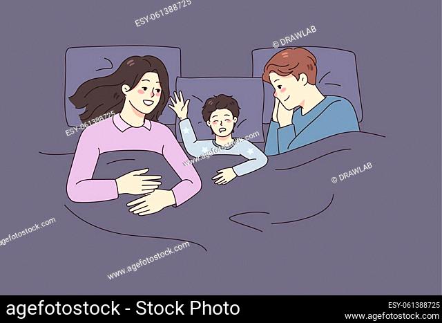 Happy young family with small kid sleep together in bed at home. Smiling parents relax take nap with little child. Childcare and parenthood concept