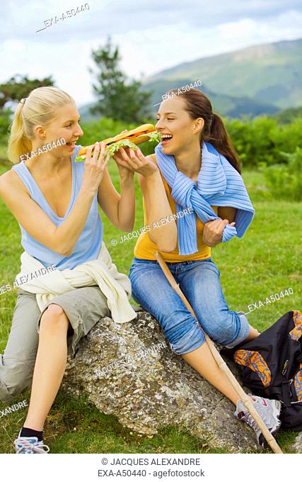 After hiking through the countryside two young women have a picnic and share a sandwich