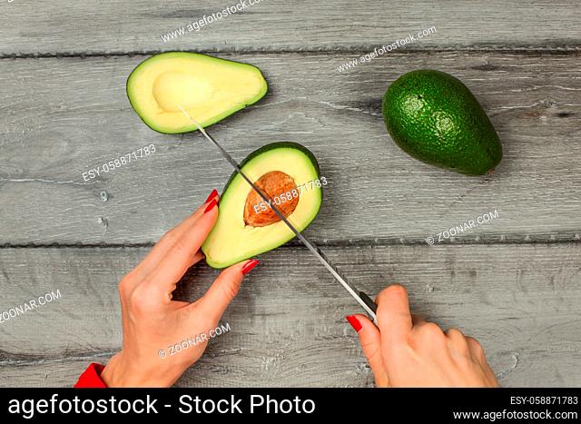 Tabletop view - woman hand holding chef knife, removing seed from avocado cut in half