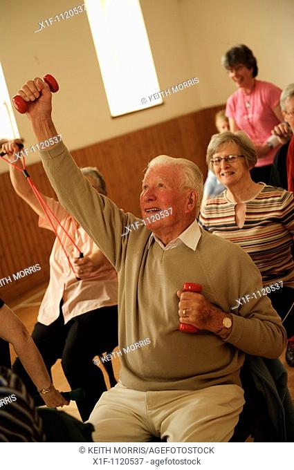 senior citizens participating in a low-impact chair aerobics class in a small village hall in west wales UK