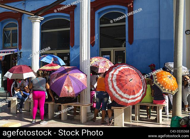 People in a waiting queue at a grocery using umbrellas as sunshades. Manzanillo, Cuba