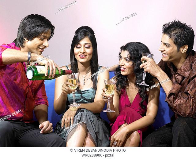 South Asian Indian man pouring champagne in glass of friend celebrating party MR