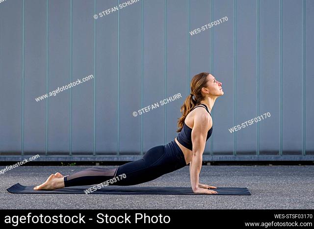 Woman practicing cobra pose in front of wall