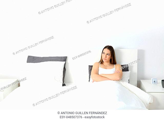 Front wide angle view portrait of an angry woman sitting on the bed looking at side with an isolated white space above