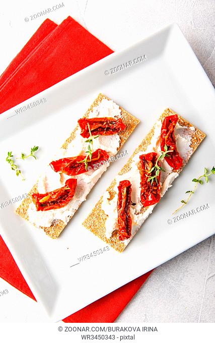 Crispbread with soft ricotta cheese and sun-dried tomatoes and thyme. Top view