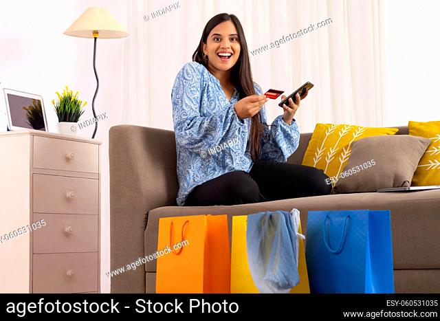 Indian girl posing in front of camera with smartphone and debit card