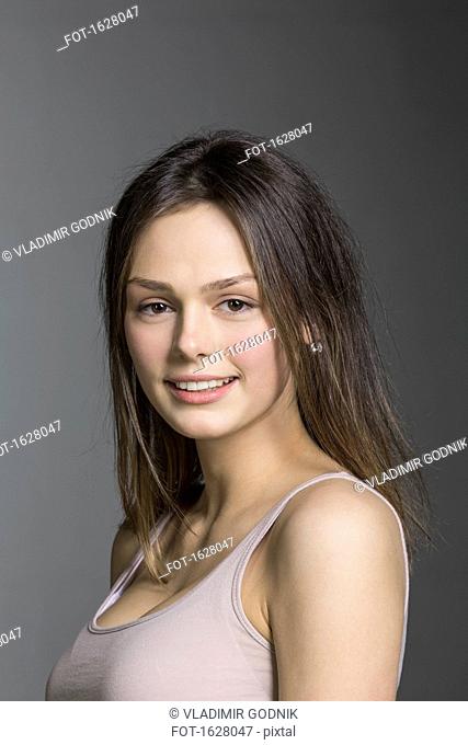 Close-up portrait of smiling young woman against gray background