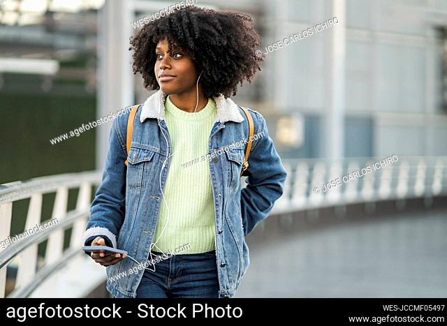 Woman with mobile phone listening music through in-ear headphones