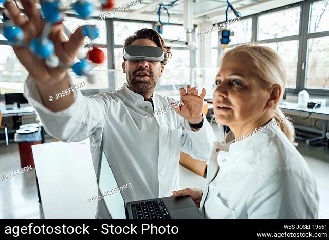 Scientist wearing virtual reality simulator examining molecular structure with colleague