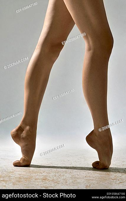 Barefoot legs of the ballerina in the studio on the gray background. She stands on the toes. Closeup. Vertical