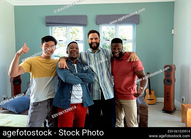 Portrait of cheerful multiracial male friends smiling while standing in living room during weekend
