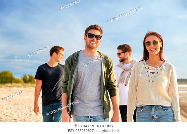 happy friends walking along summer beach