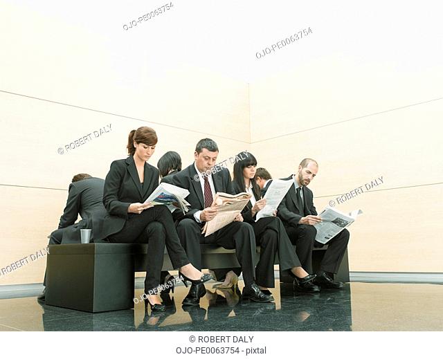 Businesspeople reading newspapers on office bench