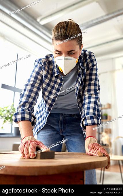 woman in respirator sanding old table with sponge
