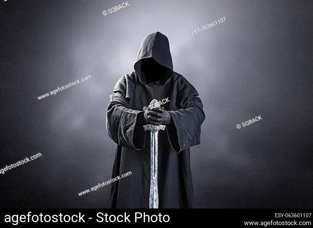 Warrior with hooded cape and medieval sword over dark misty background