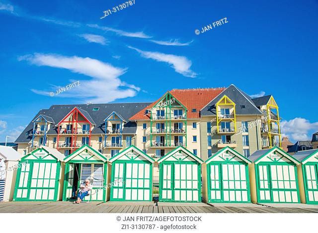 woman sitting in front of wooden cabins at the beach of Cayeux sur Mer in Normandy, France. New apartments in the back