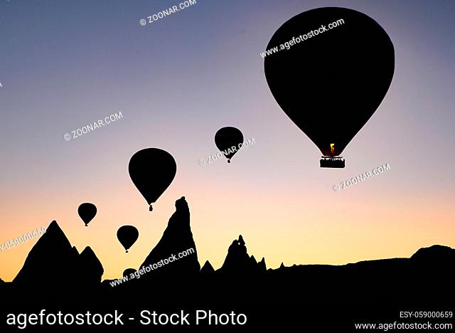 Silhouette of flying hot air balloons and rock landscape at sunrise time in Goreme, Cappadocia, Turkey