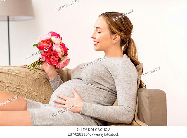 pregnancy, people, holidays and expectation concept - happy pregnant woman with flowers at home
