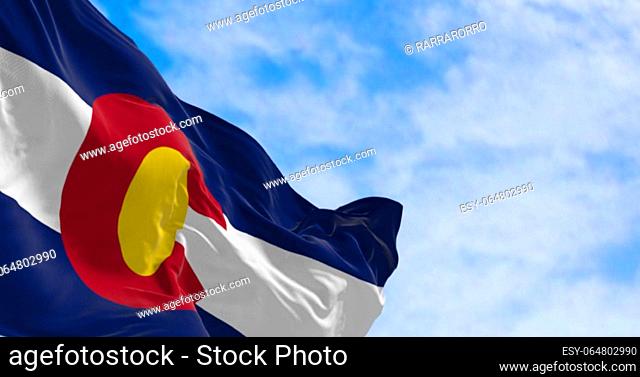 Close-up of Colorado state flag waving in the wind on a clear day. Three blue, white, and blue stripes. Red C with gold disk on top