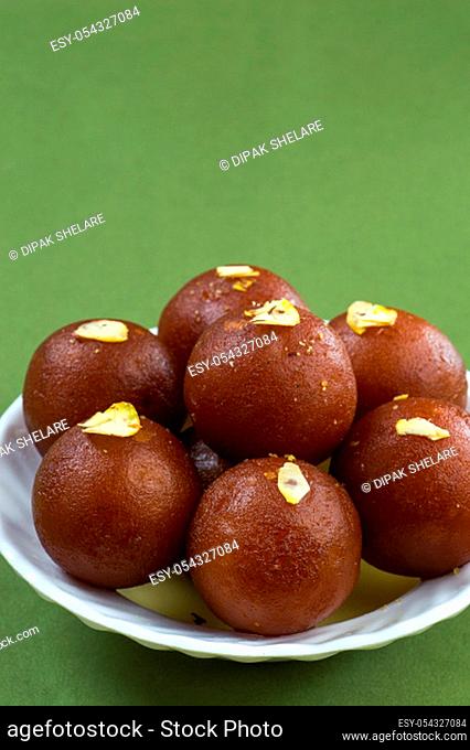 Gulab Jamun, Indian dessert topped with pistachio in white plate on green background