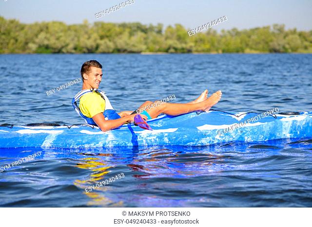Young Happy Professional Kayaker Resting in the Kayak on the River under Bright Morning Sun. Sport and Active Lifestyle Concept