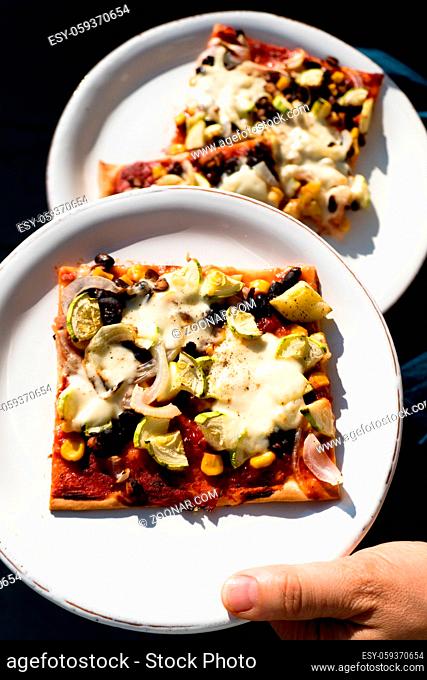 femle hand serving white plates with tasty vegetarian homemade pizza slices with fresh veggies and herbs
