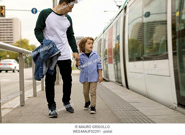 Smiling father and son walking hand in hand at tram stop in the city