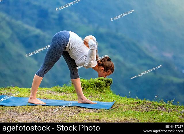 Woman doing Ashtanga Vinyasa yoga asana Parsvottanasana intense side stretch pose outdoors in mountains Himalayas. Himachal Pradesh, India, Asia