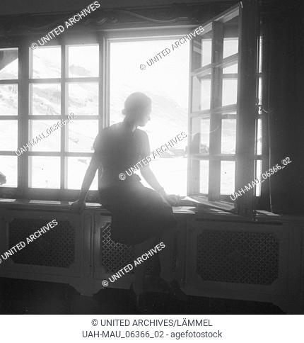 Eine junge Frau blick aus dem Fenster eines Hotels in Zürs am Arlberg, Deutsches Reich 1930er Jahre. A young woman at the window of a hotel with view to...