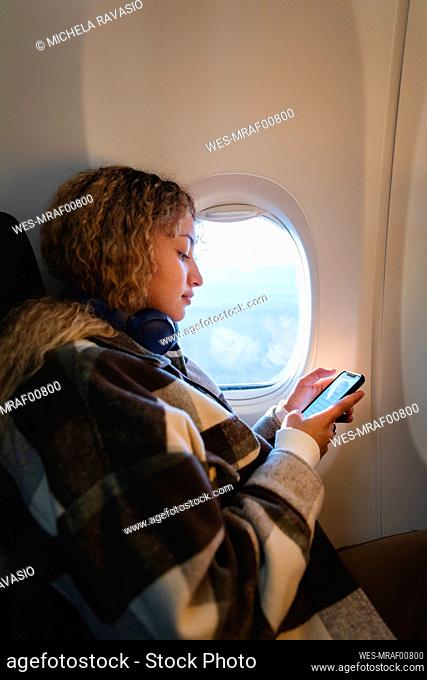 Woman using smart phone sitting near window in airplane